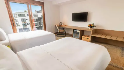Otra habitación doble con dos camas individuales, un escritorio funcional con minibar y televisión. Las ventanas ofrecen vistas a los edificios circundantes.