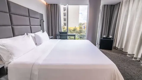 Habitación de hotel con dos camas dobles, cabeceras grises y amplios ventanales.