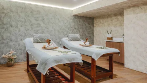 Sala de spa con dos camillas de masaje preparadas y decoración de hojas.