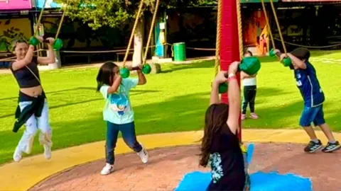 Children hanging from ropes in an amusement park.