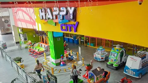 Salón visto desde arriba, en el que hay varias atraccciones mecánicas con coloridas figuras de animales y cosas. Destaca un aviso grande con una leyenda que dice: "Happy City".