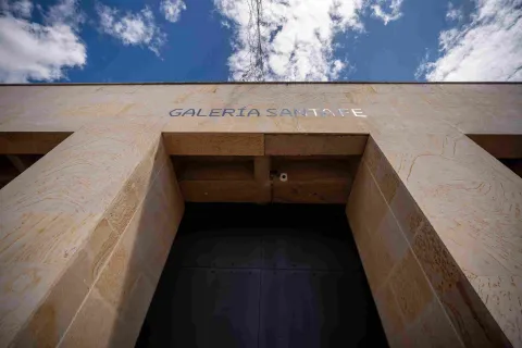 Plano de abajo hacia arriba de la fachada de edificación en piedra en la que destaca una puerta alta y negra, parece que de metal, y una leyenda sobre la parte superior que dice: “GALERÍA SANTA FE”. 