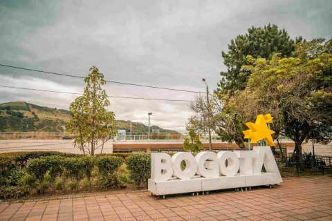 A large white sign with the word Bogotá, with yellow stars above the letter “A.” In the background, mountains can be seen.