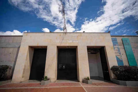 Fachada de edificación en piedra en la que destacan tres puertas negras y altas, parece que de metal, una de ellas abierta y una leyenda sobre la parte superior que dice: “GALERÍA SANTA FE”. 