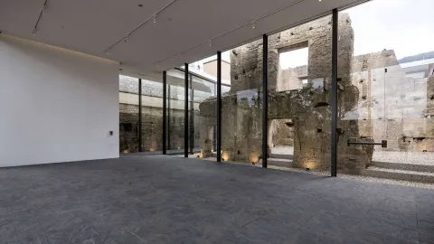 Salón grande y vacío en cuyo lado derecho hay un ventanal grande desde donde se puede ver una pared derruida.