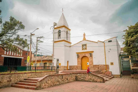Close-up of a white church with yellow accents. In front of it, there is a person wearing a red jacket.
