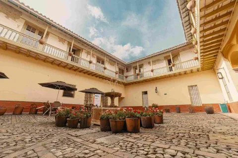 Interior de casona antigua en la que sobresalen balcones en el segundo piso. El primer piso es un patio grande y empedrado con una fuente de agua en la mitad.