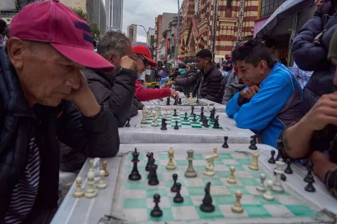 Men play chess at several tables set up on a street.