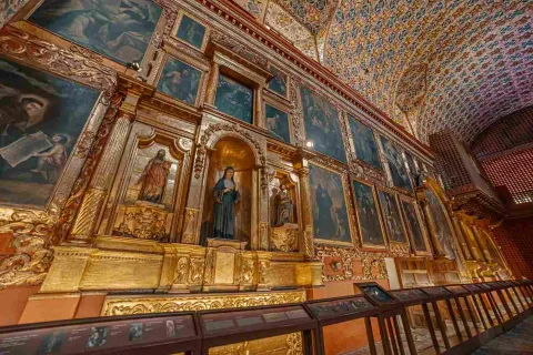 Pared abarrotada de cuadros y retablos.