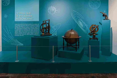 Cuatro objetos relacionados con astronomía: uno es un mapamundi redondo y en madera, y dos telescopios pequeños y metálicos. Hay un aviso con una leyenda que dice: “¿Y para qué se estudiaba astronomía?”.