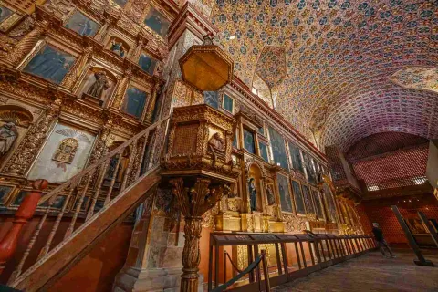Púlpito en madera delante de una pared abarrotada por cuadros y retablos.