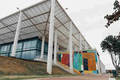 Gran estructura entre metal y vidrio. Hay una pared con imágenes de rostros de colores.