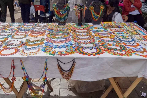 A collection of handcrafted necklaces in the colors of the Colombian flag are displayed on a table.