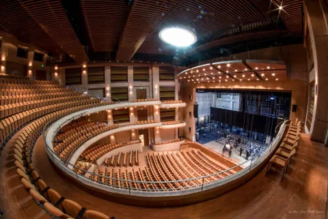 Interior of a theater, viewed from the side, with several rows of gold-colored benches arranged in a spiral.