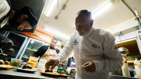 Un chef experimentado, en un uniforme blanco, emplatando con precisión un pequeño plato en una cocina.