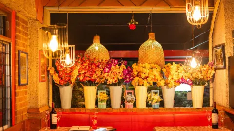 Un interior de restaurante decorado con exuberantes arreglos florales y lámparas colgantes, creando un ambiente vibrante. 