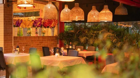  Mesas preparadas para cenar en un ambiente de restaurante con decoración cálida, luces y vegetación. al.