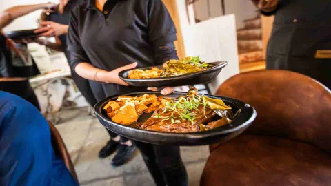 Una persona sirviendo dos platos con comidas gourmet, adornados con hierbas y acompañamientos. 