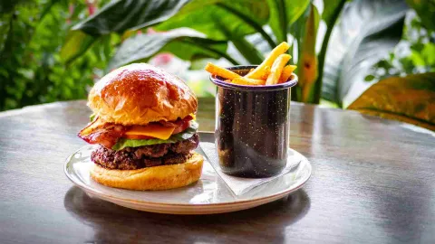 Una apetitosa hamburguesa doble con queso y tocino, acompañada de papas fritas en un recipiente esmaltado.