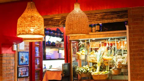 Descripción: Lámparas de mimbre colgantes en un restaurante, con detalles de decoración rústica y una vitrina de productos frescos. 