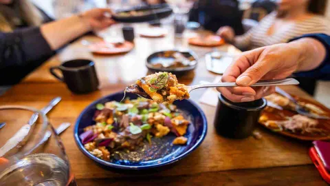 Una cuchara eleva un bocado de un platillo colorido, revelando texturas y sabores en una mesa de comedor. 