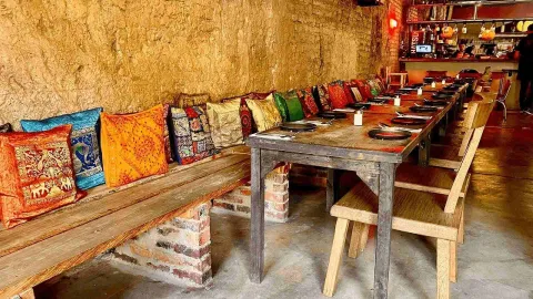 Interior de un restaurante con una larga mesa de madera y un banco corrido decorado con cojines de colores vibrantes.