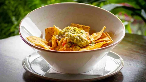 Un tazón de nachos crujientes cubiertos con queso derretido, pico de gallo y abundante guacamole fresco.