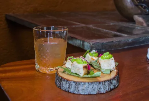 Exquisitos canapés en una tabla de madera rústica, acompañados de una bebida refrescante. 