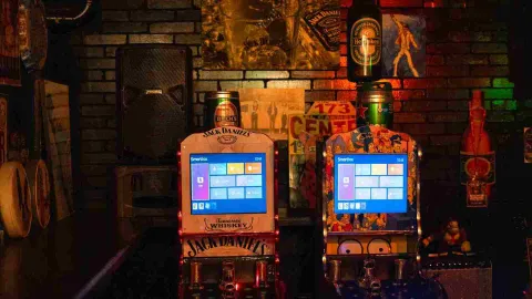 Dos máquinas recreativas digitales con temática de Jack Daniel's y Los Simpson en un bar.