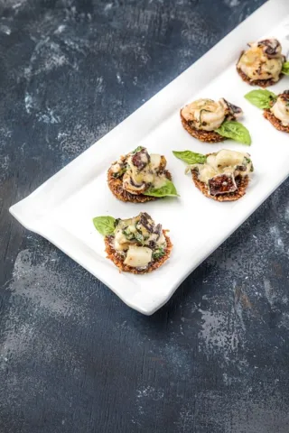 Canapés individuales elegantemente presentados con mariscos y hojas de albahaca sobre una bandeja blanca alargada. 