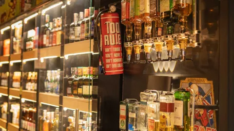 Primer plano de pollo frito y papas a la francesa en un tazón de metal, con botellas de salsa desenfocadas al fondo.
