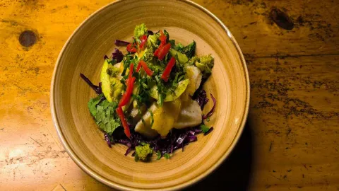 Vista cenital de un cuenco de cerámica con una ensalada colorida que incluye col lombarda, aguacate, brócoli y tiras de pimiento rojo.