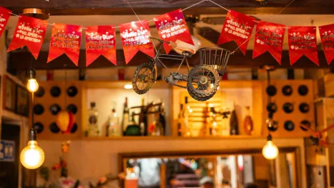 Zona de la barra del restaurante, adornada con iluminación cálida, botellas y decoración festiva colgante.