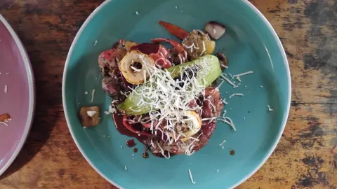  Vista cenital de un plato turquesa con una comida que consiste en carne cocinada, verduras asadas y una pizca de queso rallado.