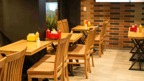 Vista de varias mesas y sillas de madera dispuestas en el interior del restaurante, listas para los clientes.
