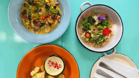 Toma cenital mostrando tres platos diferentes: mariscos con maíz, una preparación con flores comestibles y patatas.