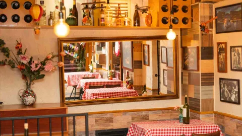 Un gran espejo de pared refleja el comedor preparado con mesas y manteles de cuadros rojos y blancos.