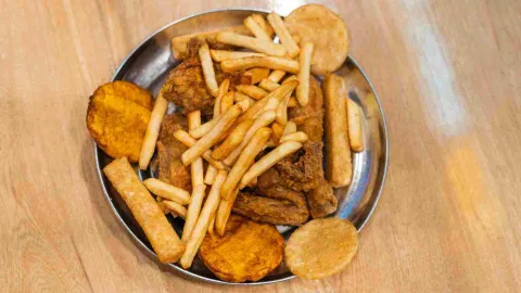  Un plato metálico grande lleno de pollo frito, papas fritas, patacones y arepas, visto desde arriba.