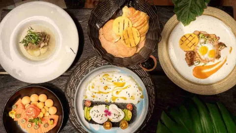 Mesa con un surtido variado de platos de desayuno, incluyendo salmón, tostadas de aguacate, huevos, arepas y caldo.
