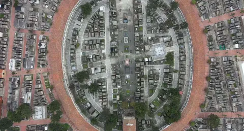 Aerial view from a drone showing a circular panorama of the central cemetery. Brick pathways, laid out in a labyrinthine style, and some trees are prominent features.