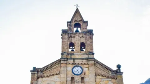 Close-up of the upper part of the stone church, highlighting the tower with its bell tower and clock.