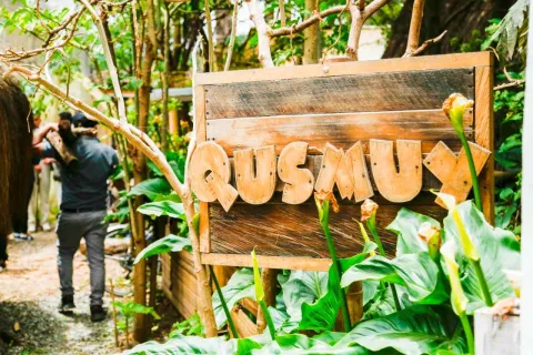 Una especie de jardín en la que sobresale una estructura de madera como un aviso y una leyenda que dice: "Qusmuy". 