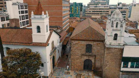 Vista desde arriba de la fachada y techo de la iglesia en tejas de ladrillo. Al lado hay otra iglesia y al fondo edificaciones.