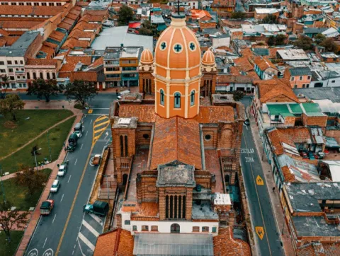 Panorámica de una iglesia vista desde arriba, como con un dron. Sobresalen los techos de ladrillo y una torre alta en forma ovalada y de color naranja.