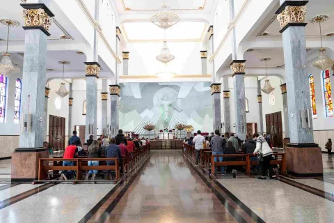 General view of the church interior, showing people kneeling and standing in prayer.