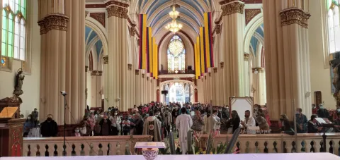 Panorámica del interior de la iglesia en la que destaca que está repleta de personas y hay unas banderas de Colombia que cuelgan en la parte alta.