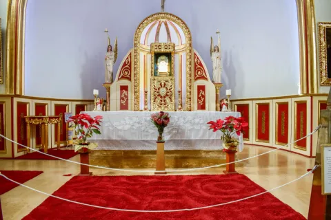 Close-up of the parish church's interior, showing the altar decorated with three floral arrangements and several red rugs.