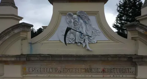 Close-up of a figure that appears to be Death, holding a black scythe, atop a facade.
