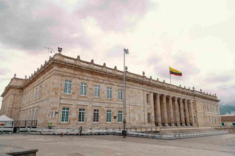 Vista lateral de la fachada del Capitolio Nacional en piedra. Se observan algunas ventanas y la bandera de Colombia izada en lo alto.