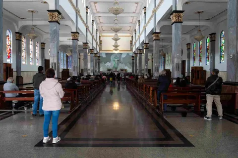 General view of the church interior. In the background, the altar with a large crucifix is ​​visible, surrounded by chairs with people.